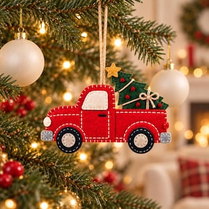 May include: A red felt truck Christmas ornament featuring a green felt Christmas tree in the truck bed, decorated with a small yellow star and red pom-poms. The truck has white stitching details, a beige window, and black wheels with beige centers.