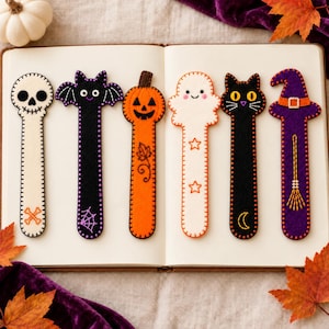 May include: Six felt bookmarks featuring Halloween designs: a white skull with crossbones, a black bat with a spiderweb, an orange jack-o'-lantern with a leaf, a white ghost with stars, a black cat with a moon, and a purple witch hat with a broom.