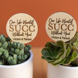 May include: Two small potted succulents with wooden signs that say "Our Life Would Succ Without You!" with the names Victor & Tanya on each sign.