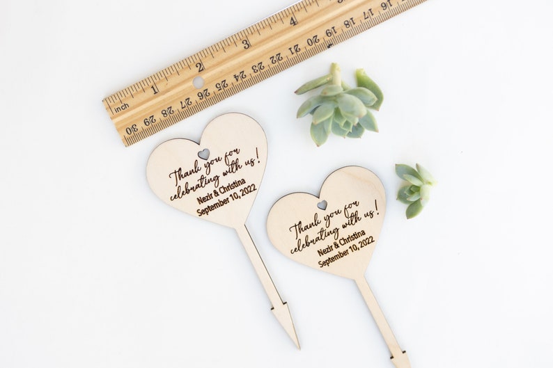 May include: Two wooden heart-shaped wedding favor signs with the text "Thank you for celebrating with us! Nezir & Christina September 10, 2022".