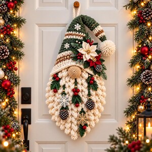 May include: A crochet gnome wall hanging featuring a tall green and white striped hat with a pom-pom, a beige nose, and a thick white textured beard. The gnome is decorated with white and red poinsettia flowers, pinecones, red berries, and snowflakes.