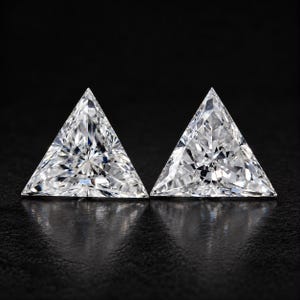 Può includere: Due pietre preziose trasparenti e incolori tagliate in una forma triangolare a trillion. Ogni pietra presenta una superficie sfaccettata brillante che riflette la luce, creando un aspetto scintillante e multisfaccettato su uno sfondo nero.