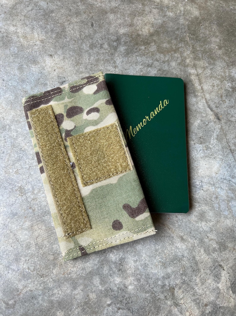 Pu&ograve; includere: Una custodia in tessuto mimetico con una cinghia in velcro e un taccuino verde con la parola "Memoranda" stampata sulla copertina.