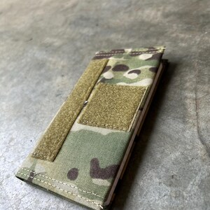 Pu&ograve; includere: Una copertina per quaderno con motivo mimetico, chiusura a velcro e una piccola tasca sul davanti. La copertina &egrave; realizzata in tessuto resistente ed &egrave; progettata per proteggere un quaderno.