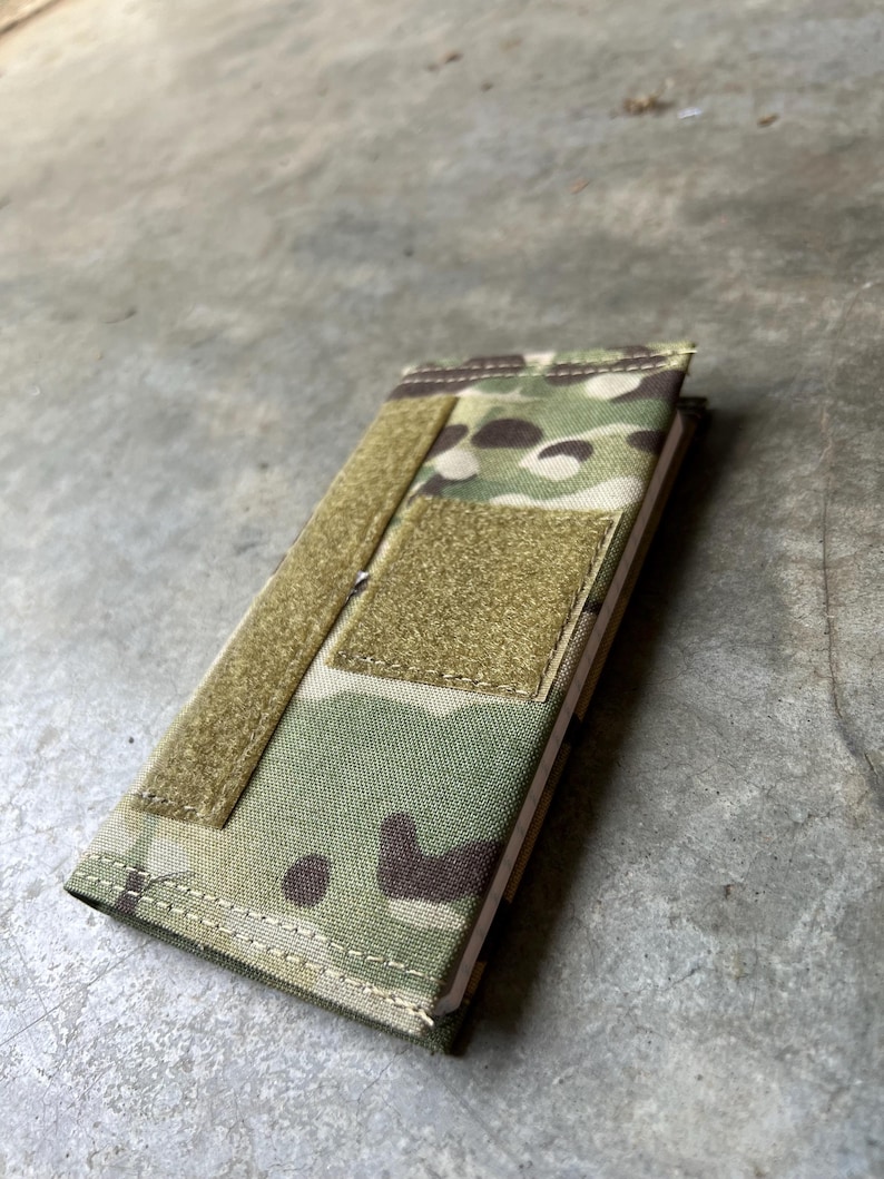 Pu&ograve; includere: Una copertina per quaderno con motivo mimetico, chiusura a velcro e una piccola tasca sul davanti. La copertina &egrave; realizzata in tessuto resistente ed &egrave; progettata per proteggere un quaderno.