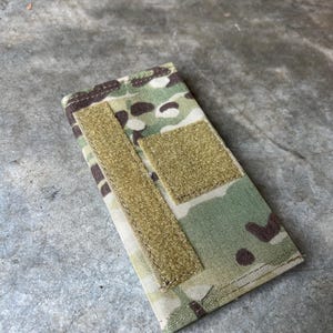 Pu&ograve; includere: Una piccola borsa mimetica con due chiusure a velcro. La borsa &egrave; realizzata in tessuto resistente e ha una combinazione di colori verde, marrone e beige.