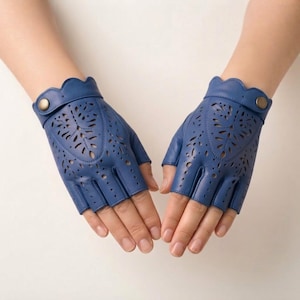 May include: A pair of blue fingerless leather gloves featuring intricate laser-cut floral patterns on the back of the hand. Each glove includes a scalloped wrist edge and a small metallic snap button closure at the side for a secure fit.