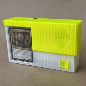 May include: A neon yellow and translucent white plastic trading card storage box featuring a vertical ribbed texture and an embossed logo. A Magic: The Gathering card titled Karlov of the Ghost Council is displayed in a clear front window slot.
