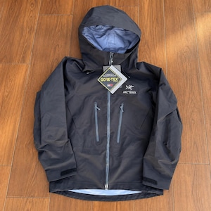 Può includere: Una giacca con cappuccio nera Arc'teryx dotata di cerniera frontale a tutta lunghezza, due tasche verticali sul petto con cerniere e polsini regolabili. Un'etichetta Gore-Tex è attaccata sul davanti e la fodera interna è di colore azzurro.