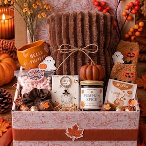 Pode incluir: Uma caixa de presente contendo uma manta castanha canelada, uma caneca laranja com o texto 'HELLO PUMPKIN', uma vela em forma de abóbora, um porta-chaves 'YOU'VE BEEN BOOED', meias com padrão de abóbora, marshmallows, um elástico e chá.