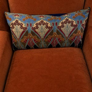 Könnte beinhalten: Ein rechteckiges Zierkissen mit einem sich wiederholenden Blumenmuster in den Farben Hellblau, Creme, Dunkelrot und Braun. Das Design besteht aus stilisierten Blumenclustern mit geschwungenen Stielen in einer symmetrischen Anordnung.