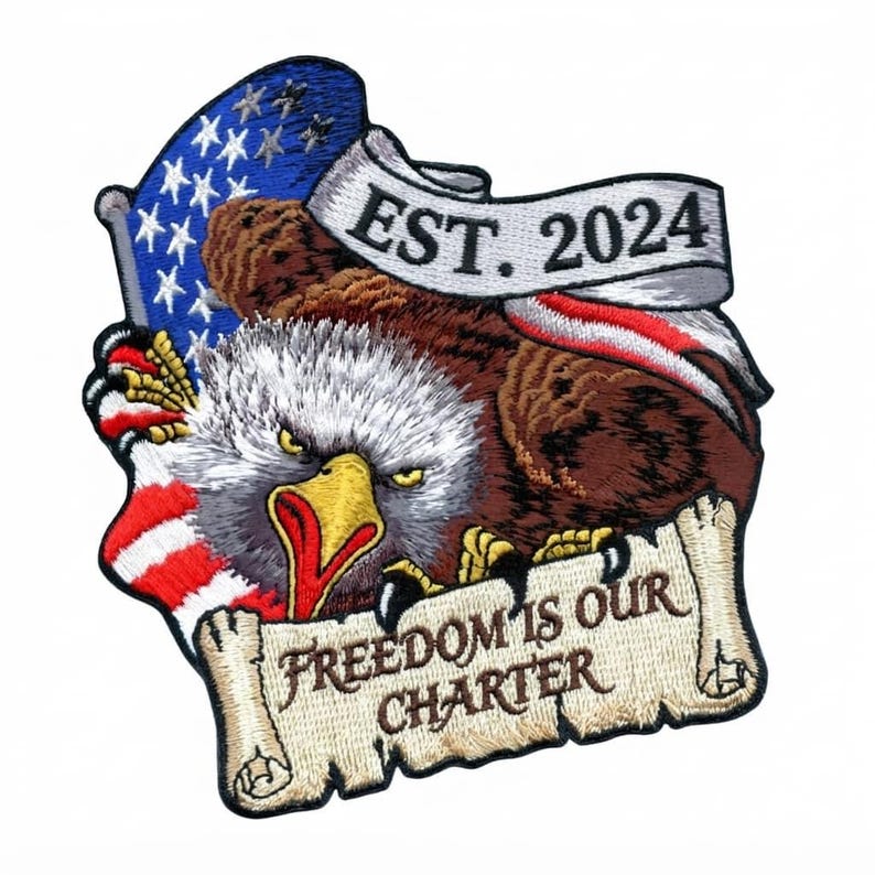 May include: An embroidered patch featuring a bald eagle with a yellow beak and brown feathers. The eagle is positioned in front of an American flag and a scroll banner that reads EST. 2024. Below the eagle is a scroll with FREEDOM IS OUR CHARTER.