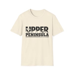 Può includere: Una t-shirt a maniche corte color crema con una stampa grafica nera sul petto. Il testo recita UPPER PENINSULA MICHIGAN, con la lettera U che contiene una silhouette della penisola superiore del Michigan e un motivo a foresta.