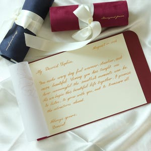 May include: A maroon folder containing a letter with gold cursive text starting with My Dearest Sophia, dated August 21, 2021, and signed Always yours, Daniel. Two fabric scrolls in navy and maroon, each tied with a white ribbon, are positioned above.