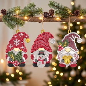 Può includere: Tre ornamenti a forma di gnomo ricamati appesi a un ramo di legno. Il primo gnomo indossa un cappello rosso con fiocchi di neve bianchi e tiene dell'agrifoglio. Il secondo indossa un cappello rosso e tiene un pupazzo di neve. Il terzo ha un cappello.