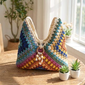 May include: A crochet hobo bag featuring a multi-colored granny square pattern in shades of blue, green, yellow, orange, and pink. The bag includes a central wooden ring accent with dangling wooden beads and two integrated shoulder straps.