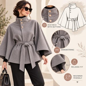May include: A grey cape jacket featuring a high neck with three light-colored buttons, wide sleeves, and a matching fabric tie belt at the waist. The design includes a technical sketch and circular detail insets highlighting the buttons and drawstring.