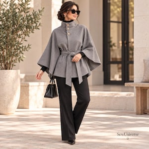 May include: A grey wool-blend cape coat featuring a high collar with three light-colored buttons, a matching tie-waist belt, and wide sleeves. The garment is worn over a black long-sleeved top and black trousers, paired with a black handbag.