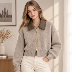 May include: A beige knit zip-up jacket featuring a contrasting dark olive green collar, long sleeves with ribbed cuffs, a matching ribbed hem, and a full-length gold-tone metal zipper closure extending from the collar to the waistline.