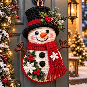 Könnte beinhalten: Ein gehäkelter Schneemann als Wandbehang mit schwarzem Zylinder mit rotem Rand, weißem Körper und rotem Schal. Der Schneemann ist mit grünen Stechpalmenblättern, roten Beeren, einem Tannenzapfen und weißen Schneeflocken-Applikationen verziert.