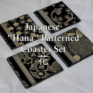 Peut inclure: Un ensemble de quatre dessous de verre carrés en ardoise noire avec des motifs floraux et linéaires dorés. Le texte "Japanese 'Hana' Patterned Coaster Set 花" est superposé sur l'image. Chaque dessous de verre a un bord texturé et brut.