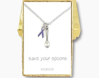 Könnte beinhalten: Eine silberne Halskette mit einem lila Band und einem Löffel-Anhänger. Die Halskette befindet sich in einer kleinen weißen Schachtel mit dem Aufdruck "save your spoons".
