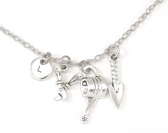 May include: Silver-toned necklace featuring gardening-themed charms. The charms include a watering can, trowel, and a wrench. A circular charm with the letter "L" is also included. The necklace is displayed on a white background.