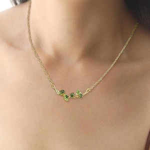 May include: A gold chain necklace with a delicate green leaf design. The leaves are arranged in a flowing pattern, creating a natural and elegant look.