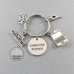 May include: A silver-toned computer science graduation keychain. The keychain includes charms with the text "GRADUATE", "2021", a laptop, a graduation cap, and a round charm with "COMPUTER SCIENCE". A 2026 charm is available.