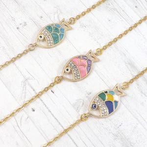 May include: Gold-toned chain bracelets with colorful fish pendants. Each fish pendant features a unique design with enamel and rhinestone accents. The fish are in shades of blue, pink, purple, green, and yellow.