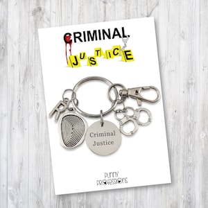 May include: A silver keychain with a fingerprint charm, a charm that says "Criminal Justice", and a pair of handcuffs. The keychain is attached to a white card with the words "CRIMINAL JUSTICE" in yellow and black letters and the words "PUNNY PROFESSIONS" in black letters.