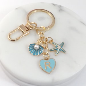 May include: Gold keychain with a blue seashell charm, a blue starfish charm, and a blue heart charm with the letter "R" on it.