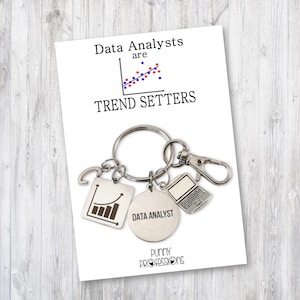 May include: A silver keychain with a graph charm, a laptop charm, and a round charm that says "Data Analyst". The card reads "Data Analysts are Trend Setters" and "Puny Professions".