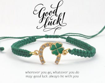 May include: Green macrame bracelet with a gold horseshoe charm and a green four-leaf clover. The horseshoe is adorned with clear crystals. The text "Good luck!" is written above the bracelet.