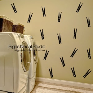May include: Black clothespin wall decals scattered on a beige wall. The laundry room scene includes a white washing machine and dryer, and two wicker baskets. The text "iSigns Decal Studio" and website address are visible.