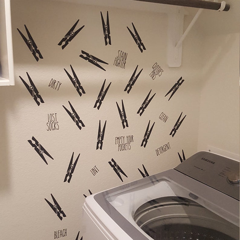 May include: Laundry room wall decor featuring black clothespin decals and text labels like "Dirty," "Clean," and "Lost Socks." The decals are scattered across the wall, creating a playful and functional design element near a washing machine.