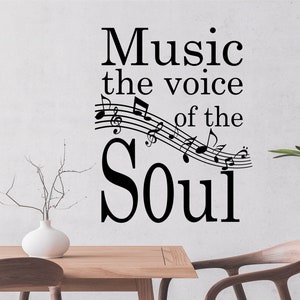 May include: Black and white wall decal with the text "Music the voice of the Soul" and musical notes. The decal is on a white wall with a wooden table and chairs in the foreground.