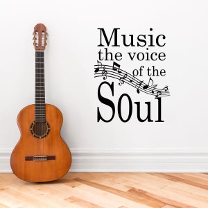 May include: A black and white wall decal with the text "Music the voice of the Soul" and musical notes. A brown acoustic guitar is leaning against a white wall.