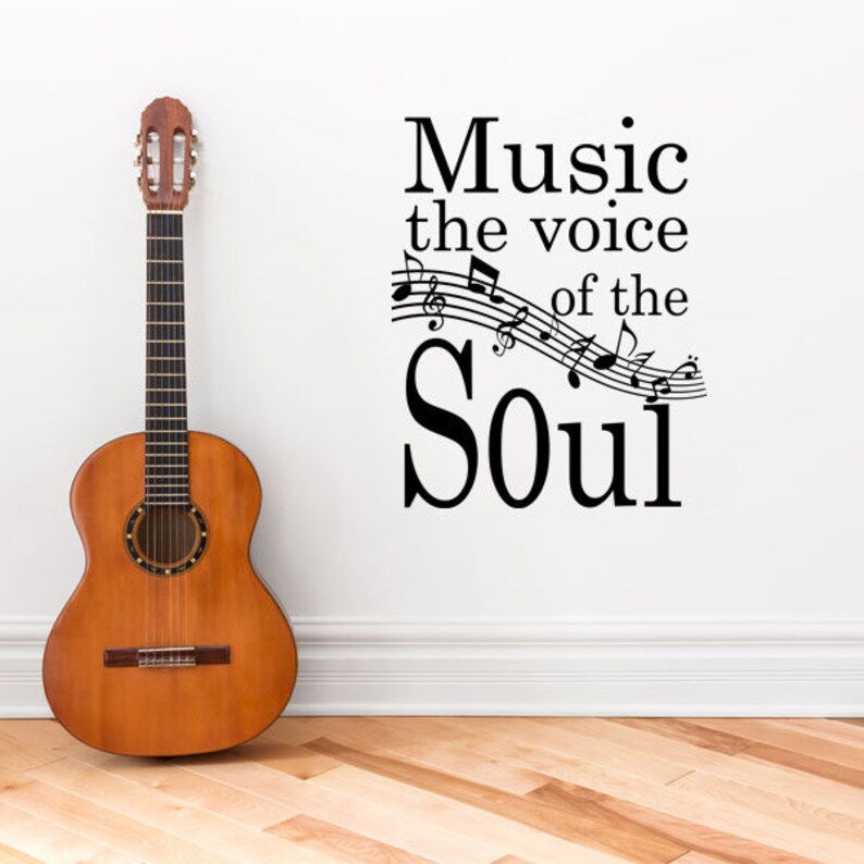 May include: A black and white wall decal with the text "Music the voice of the Soul" and musical notes. A brown acoustic guitar is leaning against a white wall.