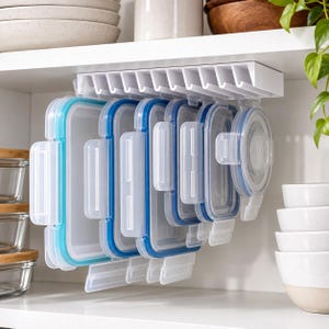 May include: A white plastic under-shelf storage organizer holds multiple rectangular and circular food storage lids. The lids feature blue and light blue silicone seals and clear plastic bodies, hanging vertically from the mounted rack.