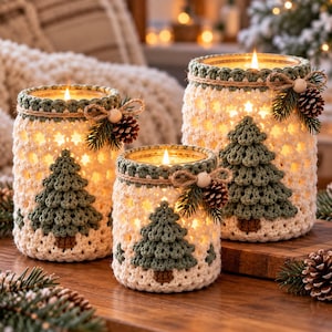 May include: Three glass candle holders wrapped in cream-colored crochet covers with green crocheted pine tree appliques. Each jar features a green crochet rim, a jute twine bow, a small wooden bead, and a miniature pinecone with green needles.