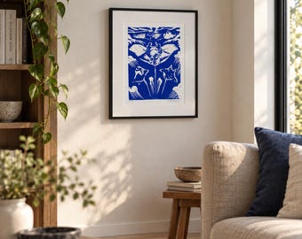 May include: A framed wall art print featuring a blue and white linocut style illustration of a manta ray swimming through stylized ocean waves. The artwork is enclosed in a simple black frame with a white mat board, hanging on a plain wall.