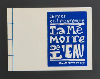 May include: A rectangular off-white booklet bound with blue thread along the left edge. The front cover features a blue rectangular block with white text reading La mer en linogravure, La Mémoire de l'EAU, and the signature PoPownc3 at the bottom.