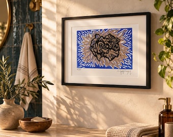 May include: A framed art print featuring a stylized black and tan floral motif centered on a vibrant blue background with radiating lines. The artwork is enclosed in a simple black frame with a white mat, displaying a signature and edition number.