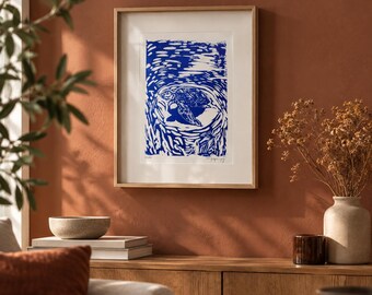 May include: A framed art print featuring a blue and white linocut style illustration of a sea turtle swimming in water. The artwork is enclosed in a light-colored wooden frame with a white mat, displaying a textured, high-contrast graphic design.