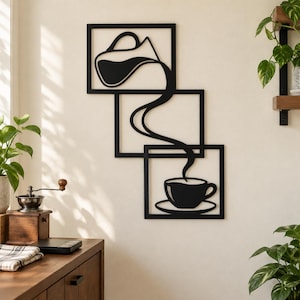 May include: A black metal wall art piece consisting of three overlapping rectangular frames. The design features a continuous line art graphic of a coffee pot pouring liquid into a coffee cup and saucer, creating a cohesive visual flow.