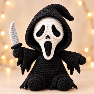 May include: A crocheted doll featuring a black hooded robe and a white mask with black eye and mouth cutouts. The figure holds a small, light gray crocheted knife in its right hand, with a textured, yarn-based construction throughout.