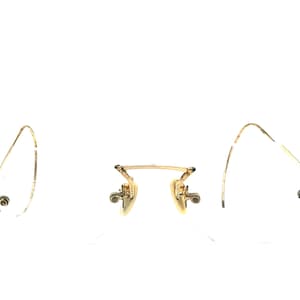 May include: A pair of vintage gold-toned eyeglasses with a delicate wire frame. The glasses feature a classic design with curved temples and nose pads. The lenses are missing, showcasing the frame's intricate details against a white background.