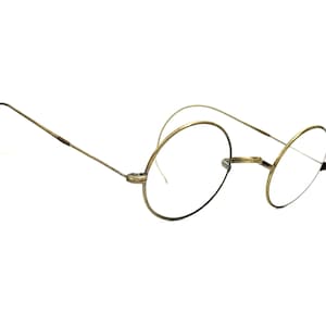 Puede incluir: Gafas redondas antiguas con monturas finas de alambre dorado. Las gafas tienen un diseño clásico y minimalista, con lentes circulares y patillas curvas para un ajuste cómodo. La estética general es vintage y elegante.