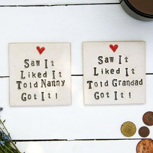 Left: Square white coaster with red heart at the top and black text; Saw It Liked It Told Nanny Got It!
Right: Square white coaster with red heart at the top and black text; Saw It Liked It Told Grandad Got It!